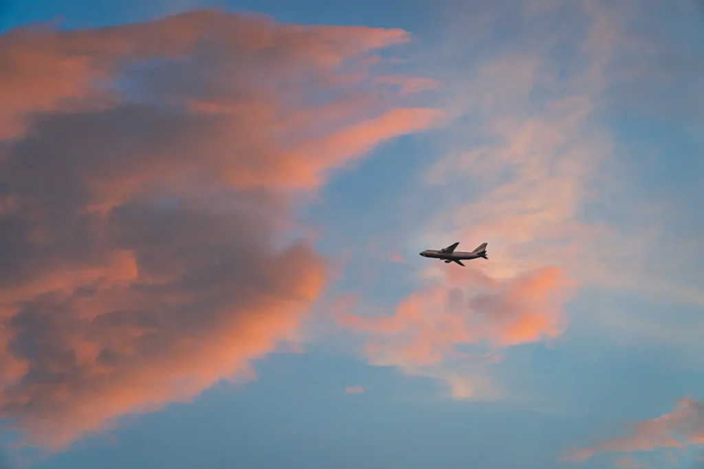 Passenger view of airplane wing soaring through clouds at golden sunset