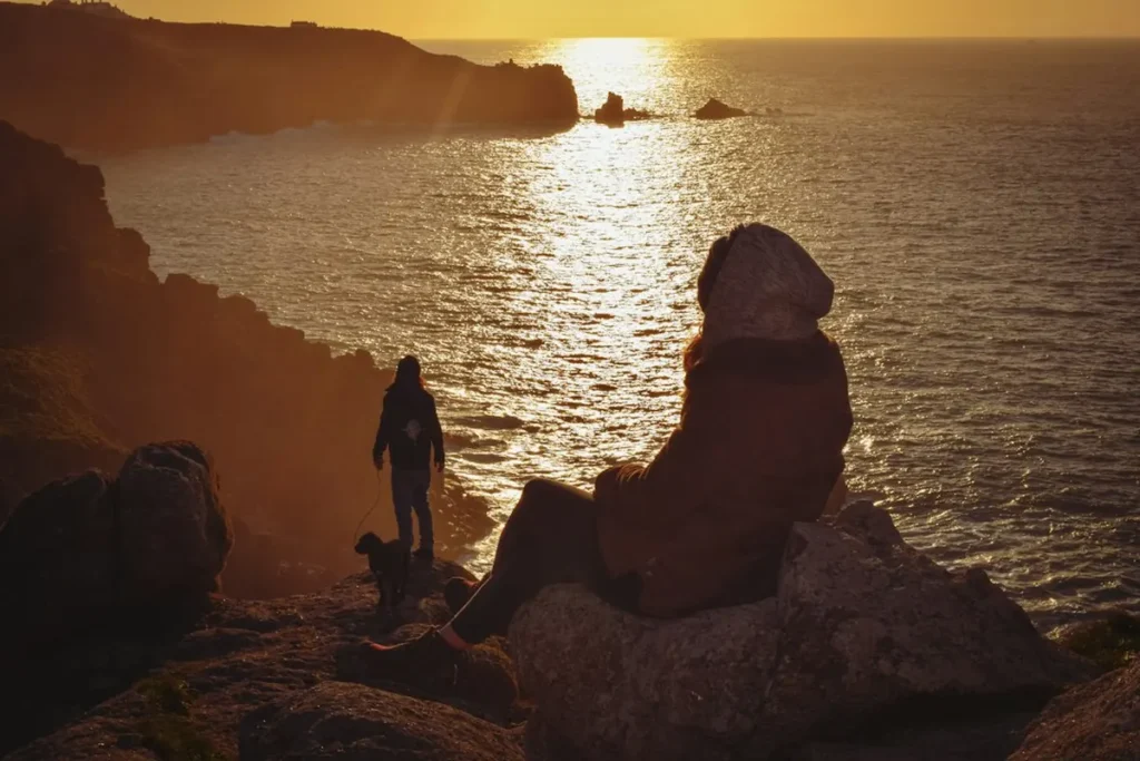 Traveler sitting peacefully on coastal cliff watching sunset over the ocean